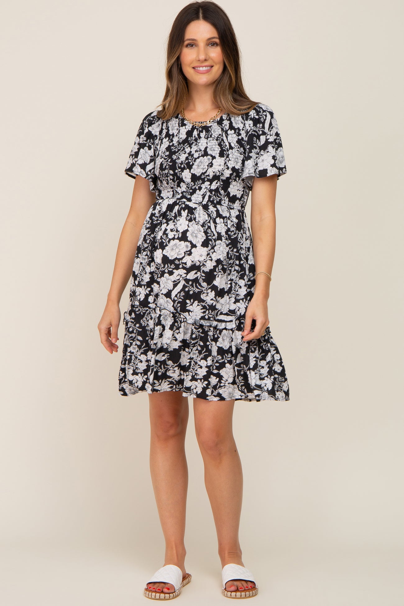woman wearing a black floral maternity dress with short sleeves and a ruffled hem, showcasing her baby bump