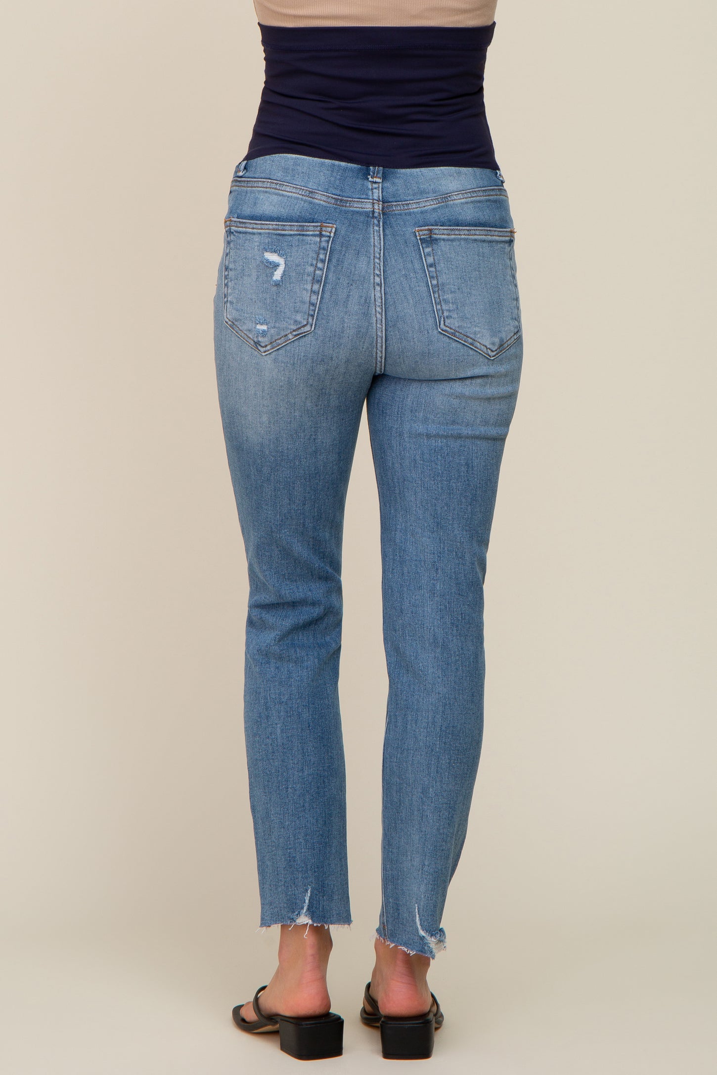 Rear view of woman wearing light wash distressed straight leg jeans with raw hem and black sandals