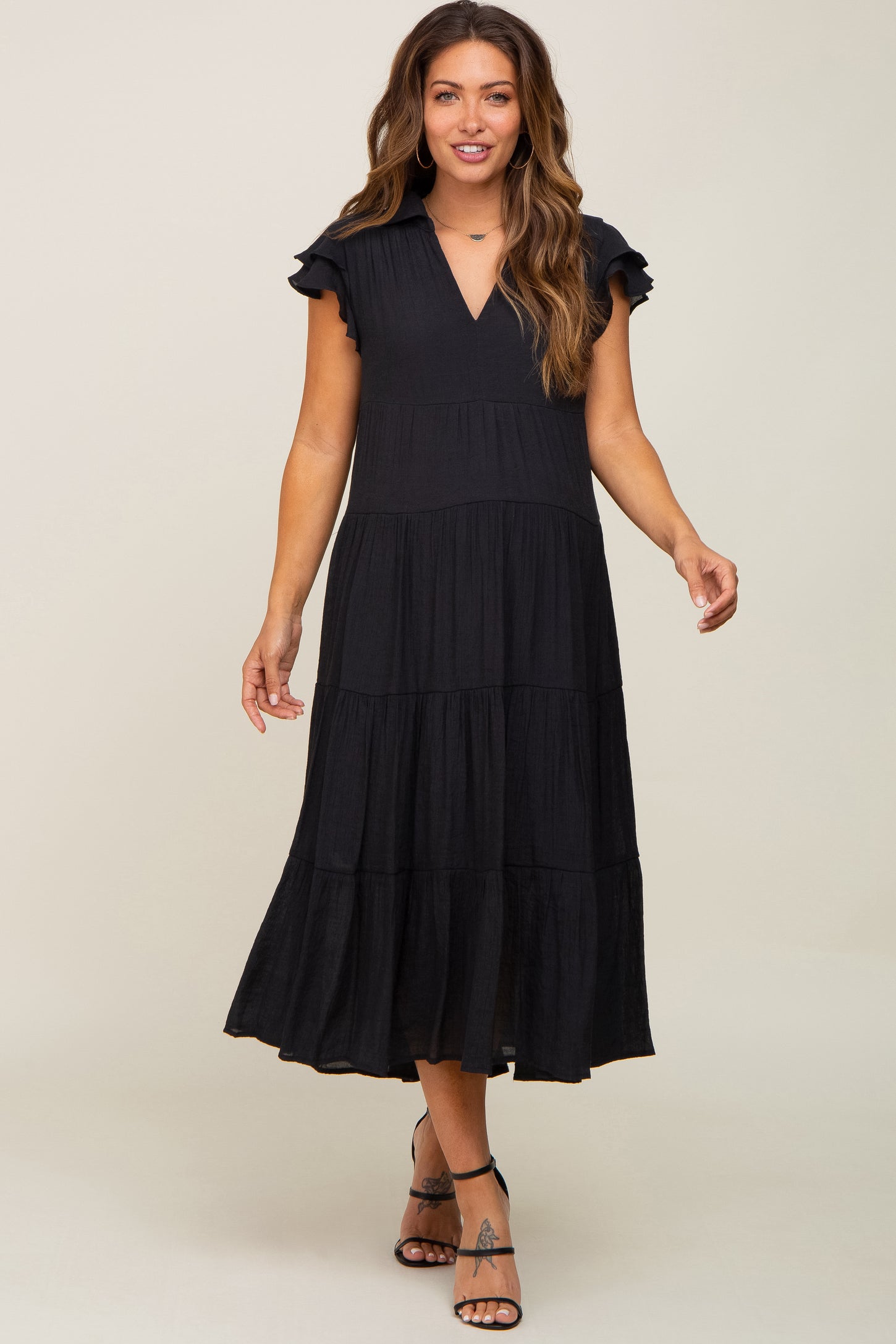 woman wearing a black tiered midi maternity dress with ruffle sleeves and a v-neckline