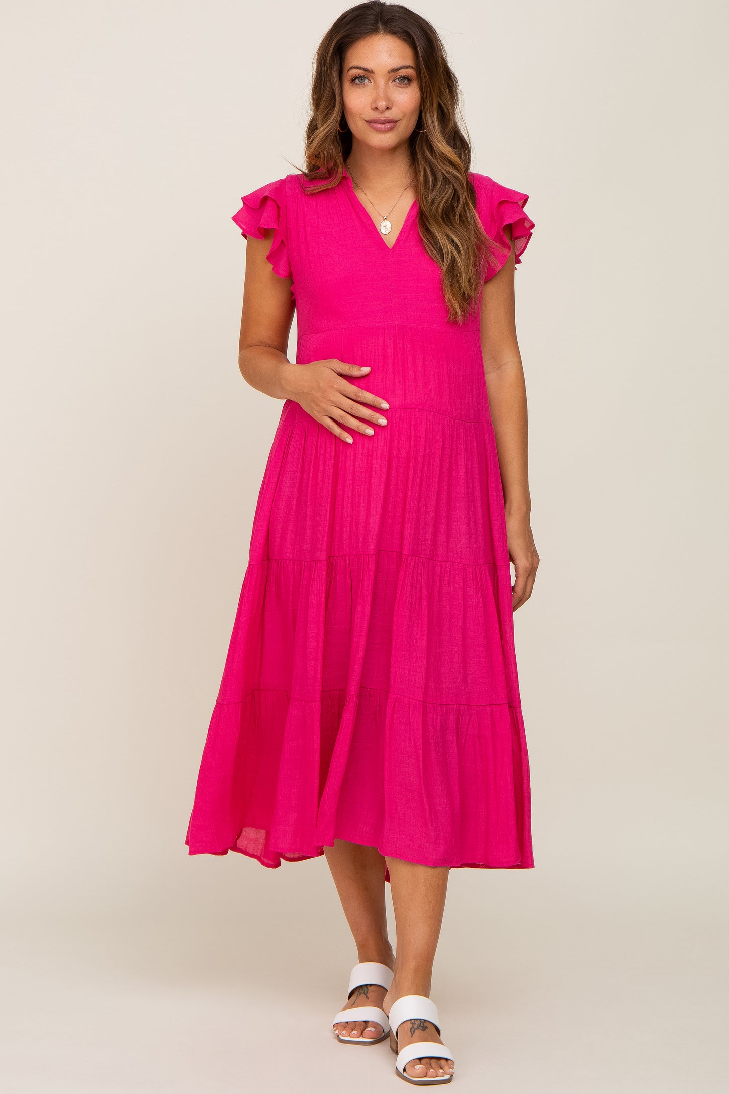 Pregnant woman wearing a hot pink tiered maternity midi dress with ruffle sleeves and white sandals
