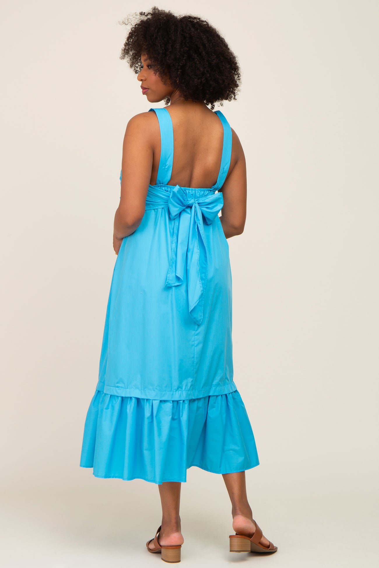 woman wearing a blue sleeveless dress with a tie back and ruffle hem, shown from the back