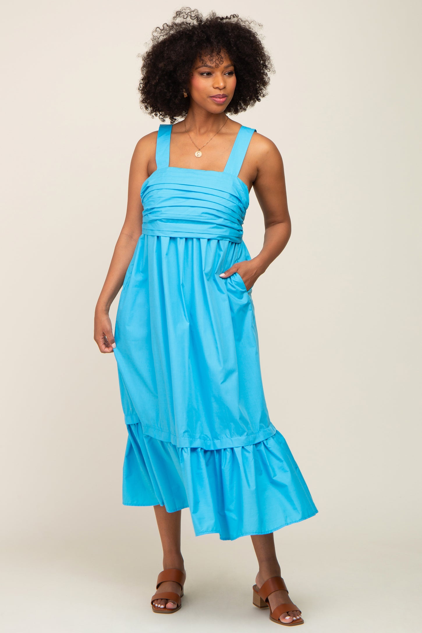 woman wearing a bright blue sleeveless midi dress with a ruffled hem and side pockets