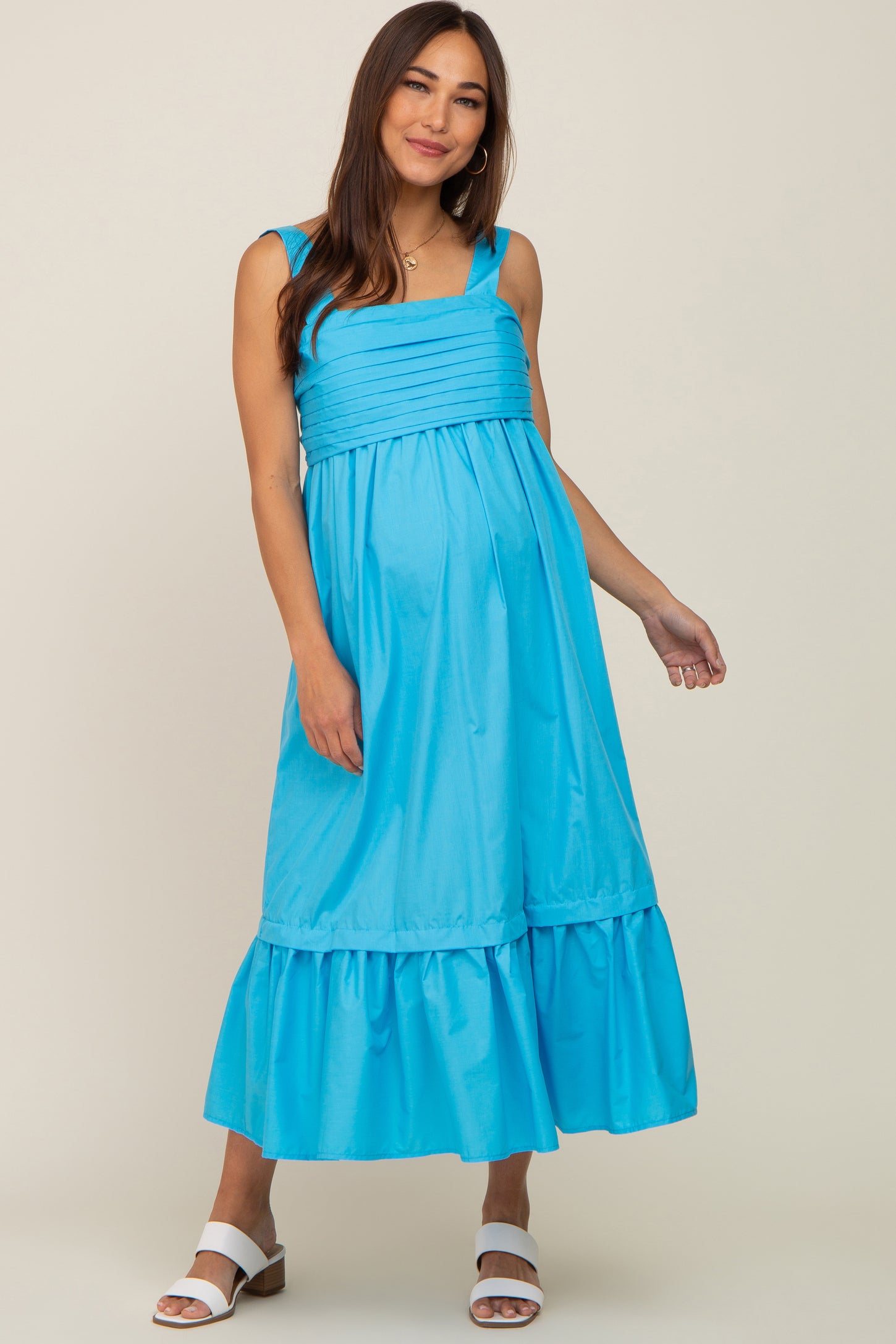 woman wearing a bright blue maternity maxi dress with tiered ruffle hem and fitted bodice, showcasing her baby bump