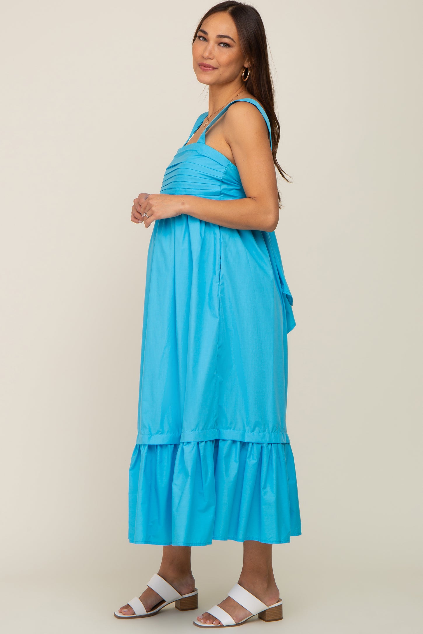 woman wearing a bright blue sleeveless maternity midi dress with ruffle hem and white sandals