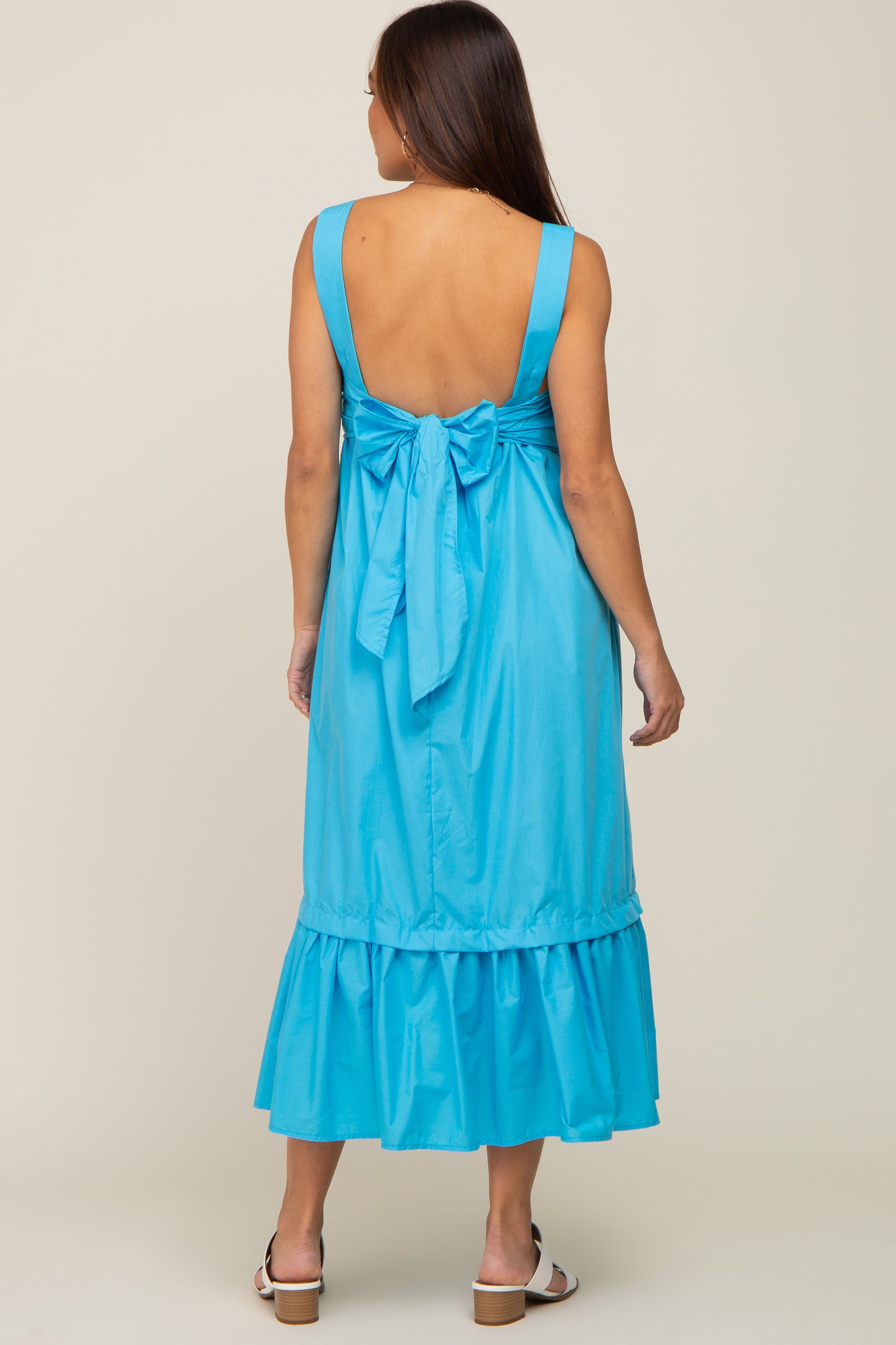 woman wearing a light blue maternity dress with a bow detail at the back and a ruffled hem