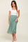 woman wearing white short sleeve top and green floral pleated midi skirt with white sandals