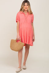 woman wearing a coral short sleeve maternity dress with tiered styling and buttons, holding a straw bag