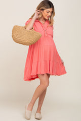 woman wearing a coral maternity dress with tiered design and holding a straw bag, baby bump visible