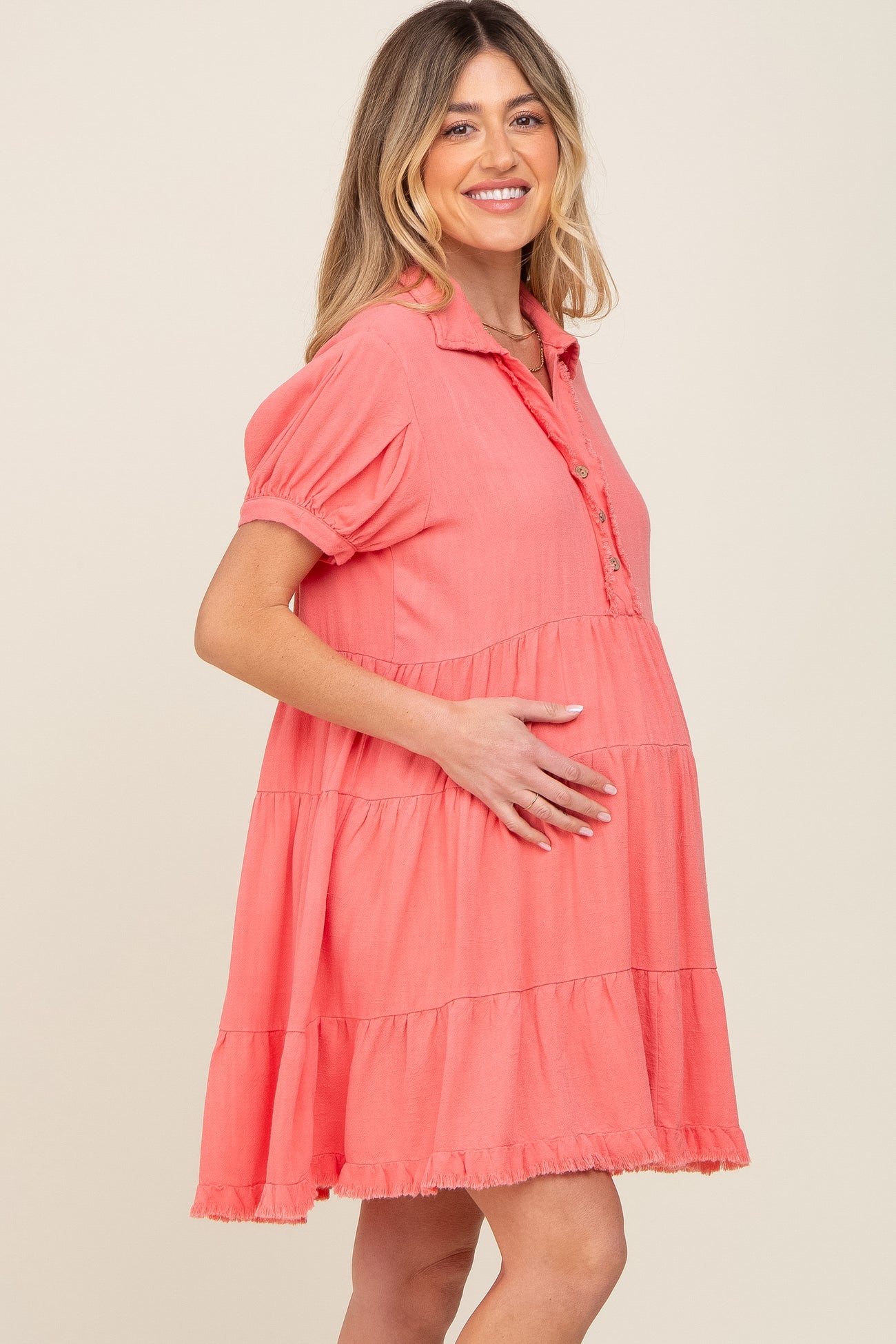 woman wearing a coral short sleeve maternity dress with a button-up front and tiers, showcasing her baby bump