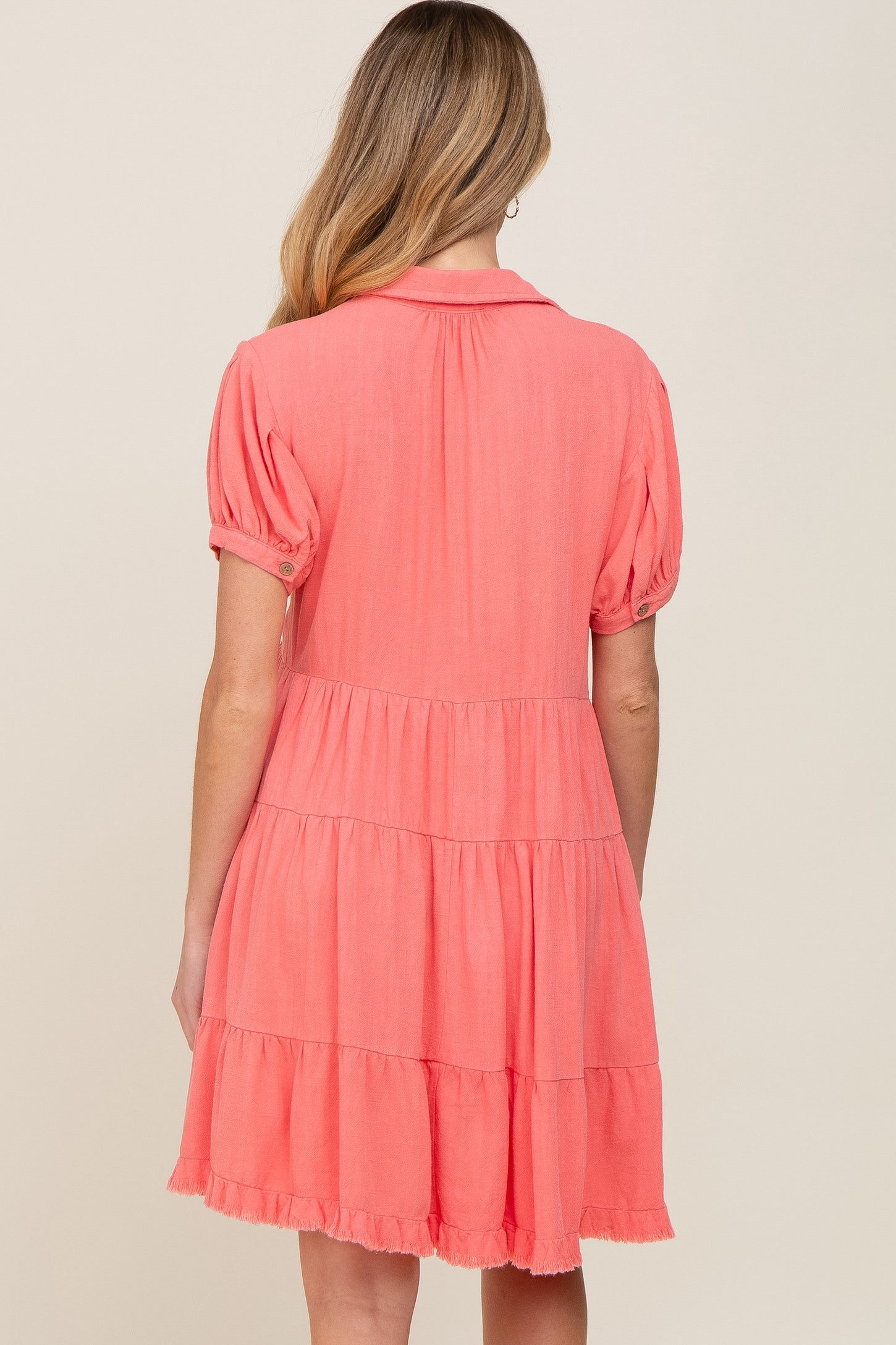woman wearing a coral pink maternity dress with puff sleeves and tiered skirt, showing the back view