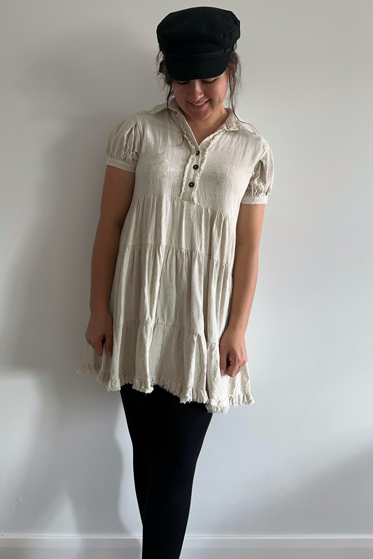woman wearing a cream tiered linen babydoll dress with puff sleeves and a black captain hat