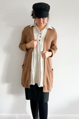 woman wearing a brown knit cardigan over a white tiered tunic dress and black baker boy hat
