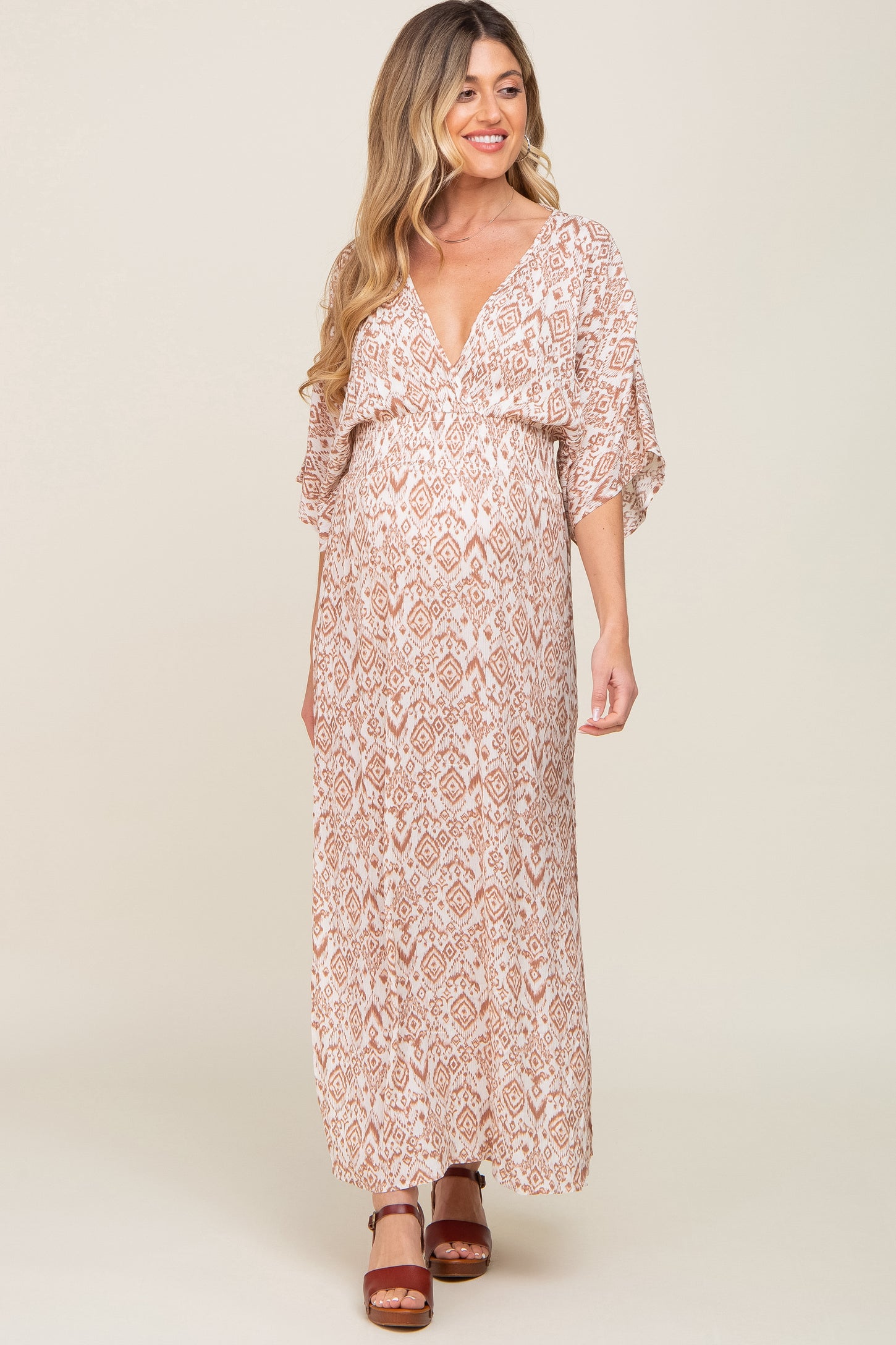 pregnant woman wearing a tan and white ikat print maternity maxi dress with a v-neckline and short sleeves