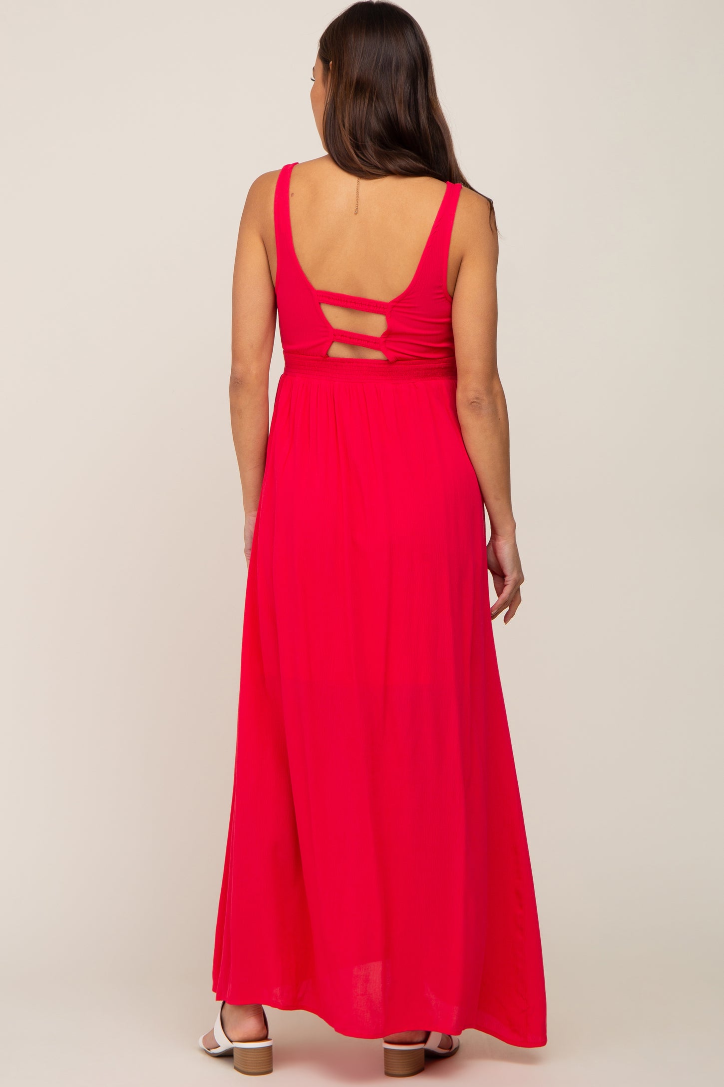 woman wearing a bright pink maternity maxi dress with cut-out back details