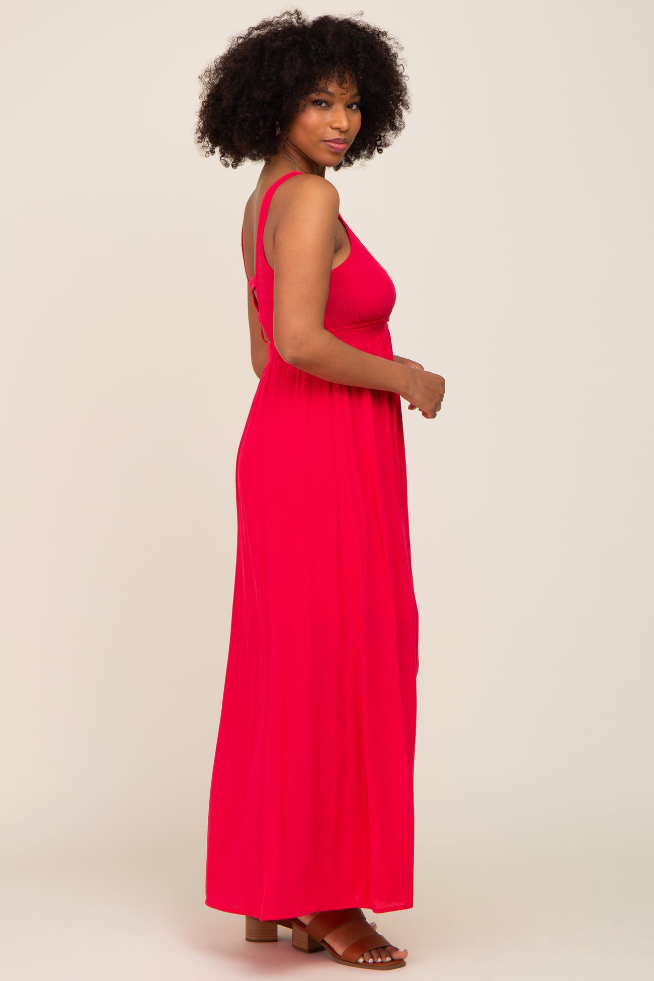woman wearing a bright pink sleeveless maxi dress with a flowing silhouette and back detail, standing in profile