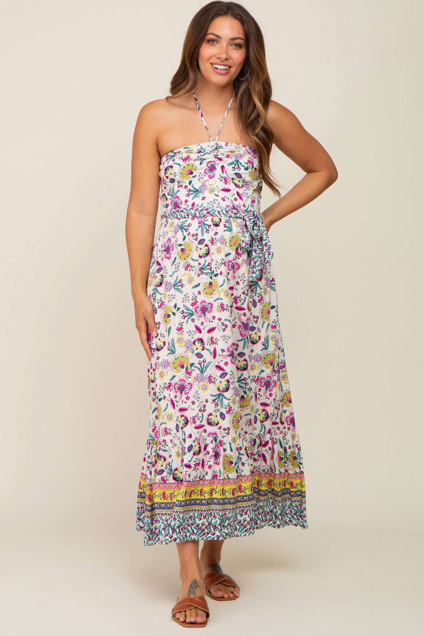 woman wearing a white floral halter neck maternity maxi dress with a belted waist and ruffled hem