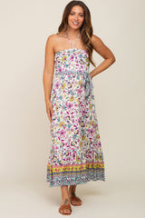 woman wearing a white floral halter neck maternity maxi dress with a belted waist and ruffled hem