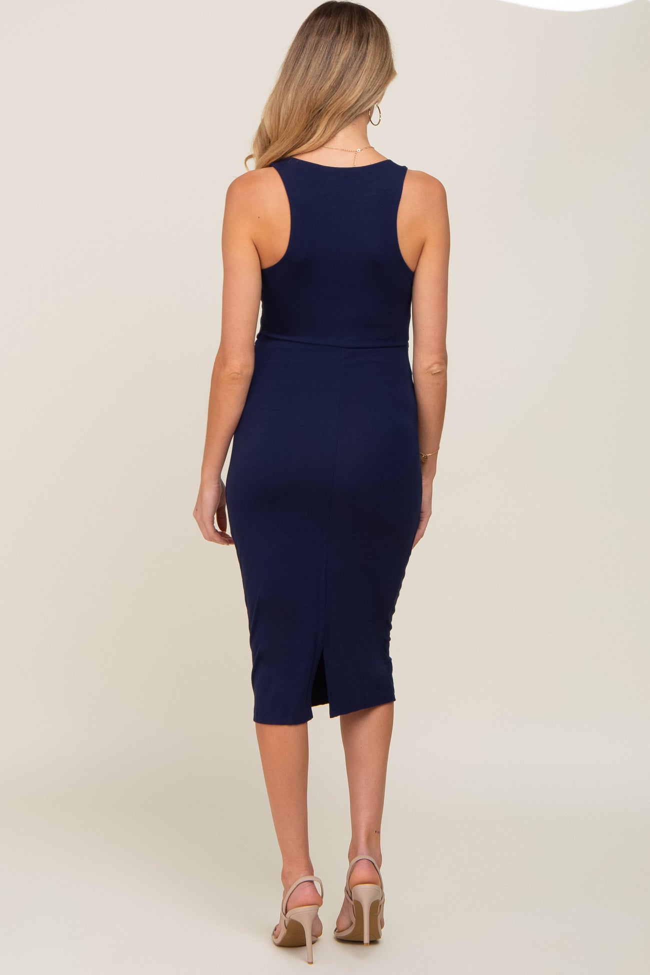 woman wearing a navy blue sleeveless maternity dress with a fitted silhouette and a back slit detail.