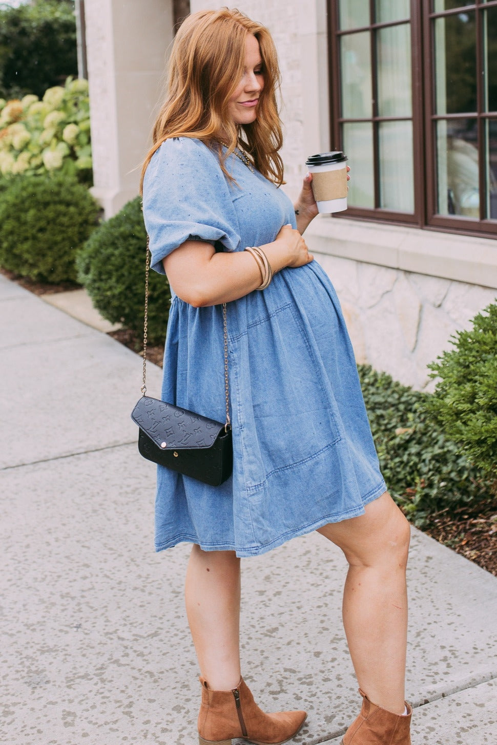 woman wearing a light blue maternity dress with short sleeves and a baby bump, holding a coffee cup