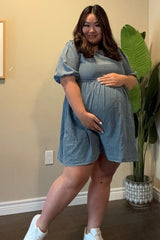 pregnant woman in blue denim maternity dress and white sneakers posing with hands on belly
