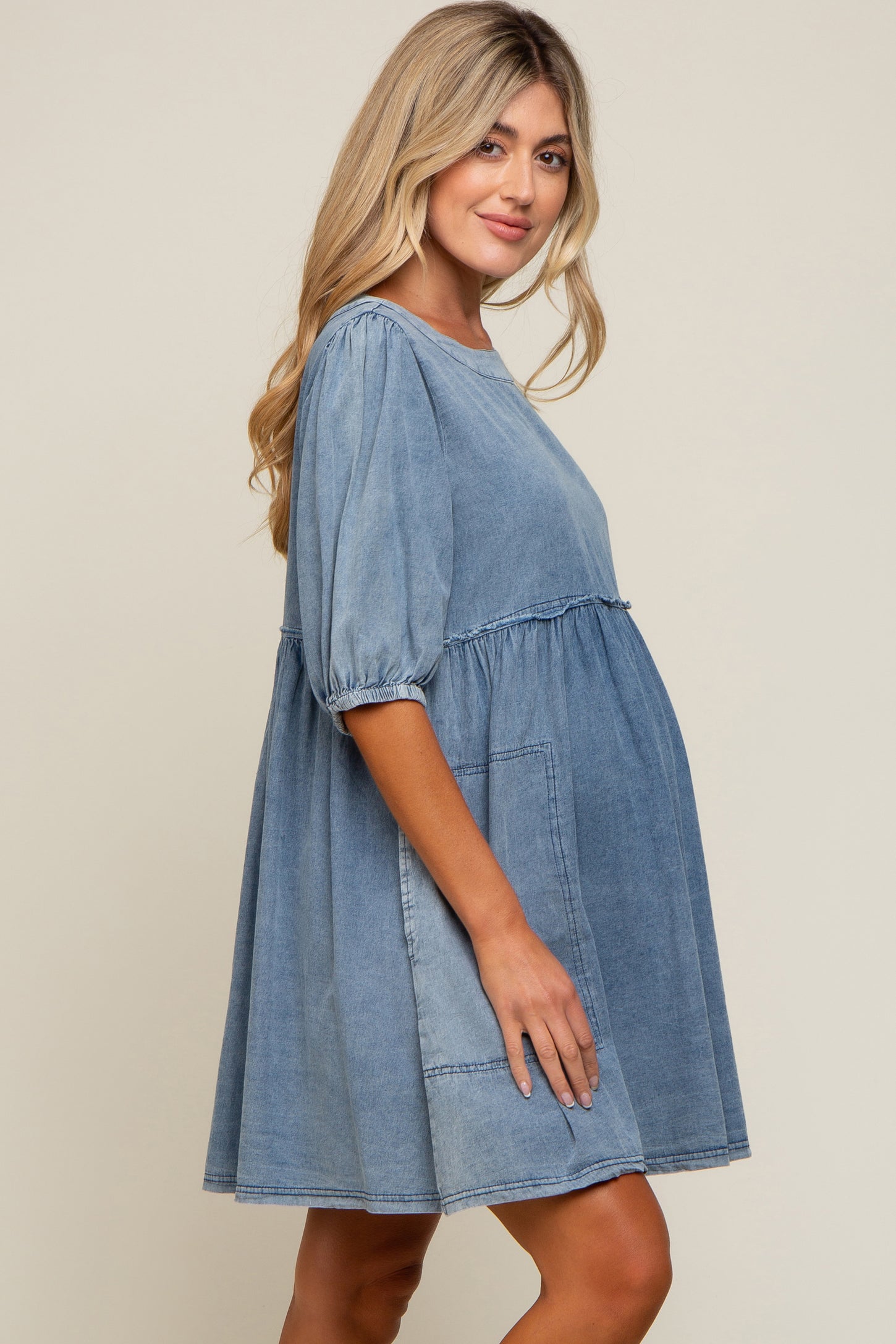 woman wearing a light blue denim maternity dress with short puff sleeves and a flowy skirt, showing her baby bump