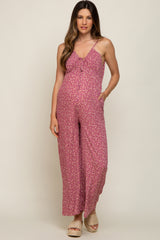 woman wearing a pink floral maternity jumpsuit with a tie front and wide legs, showcasing her baby bump