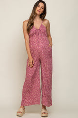 woman wearing a pink floral maternity jumpsuit with adjustable straps and pockets, showcasing her baby bump