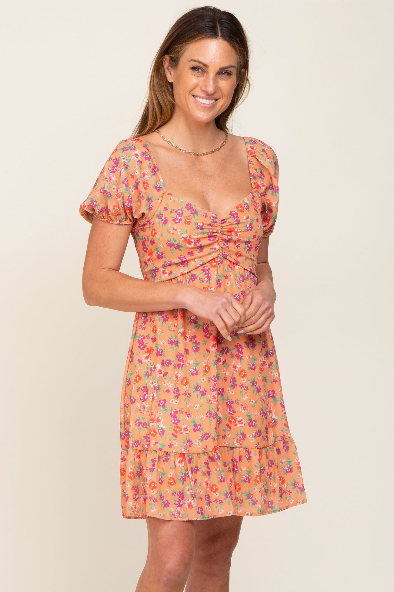 woman wearing an orange floral print mini dress with puff sleeves and a sweetheart neckline