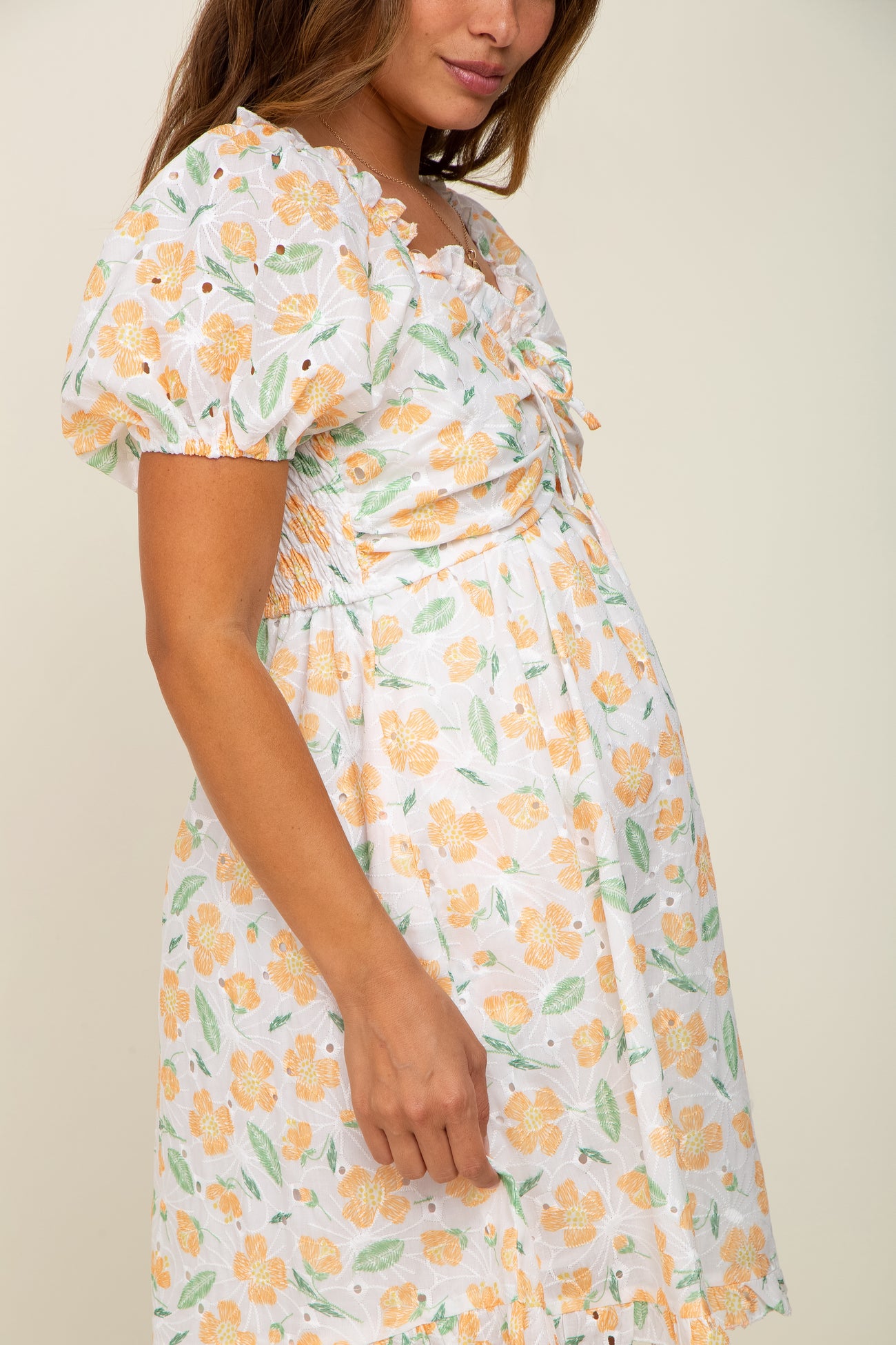 Pregnant woman wearing a white maternity dress with orange floral eyelet embroidery and puff sleeves.