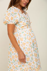 Pregnant woman wearing a white maternity dress with orange floral eyelet embroidery and puff sleeves.