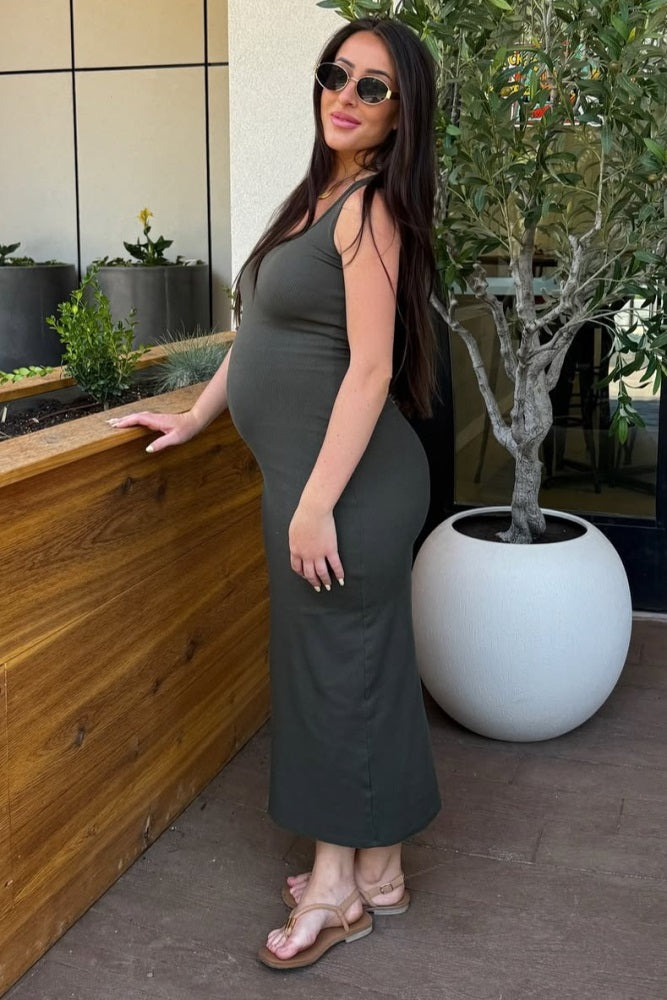 woman wearing a dark green maternity maxi dress and showing her baby bump while posing outdoors