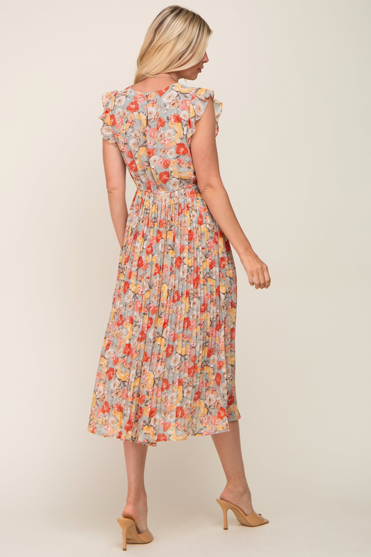Woman wearing a floral pleated midi dress with ruffle sleeves and tan heels seen from the back