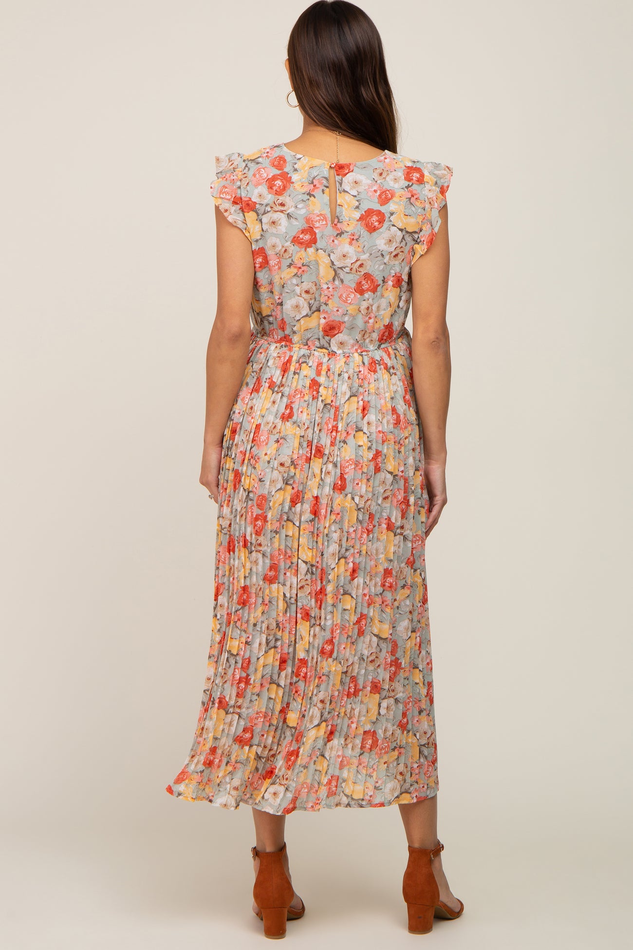 Back view of woman wearing a floral pleated midi dress with ruffle sleeves and brown block heel sandals