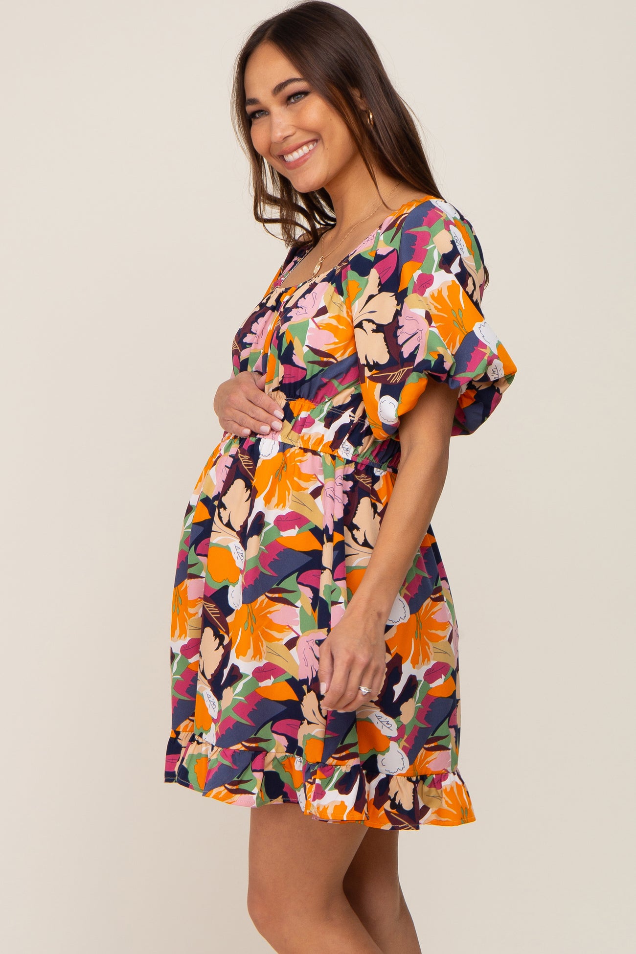 Smiling pregnant woman wearing a colorful floral maternity mini dress with puff sleeves and a ruffled hem