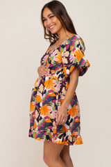 Smiling pregnant woman wearing a colorful floral maternity mini dress with puff sleeves and a ruffled hem