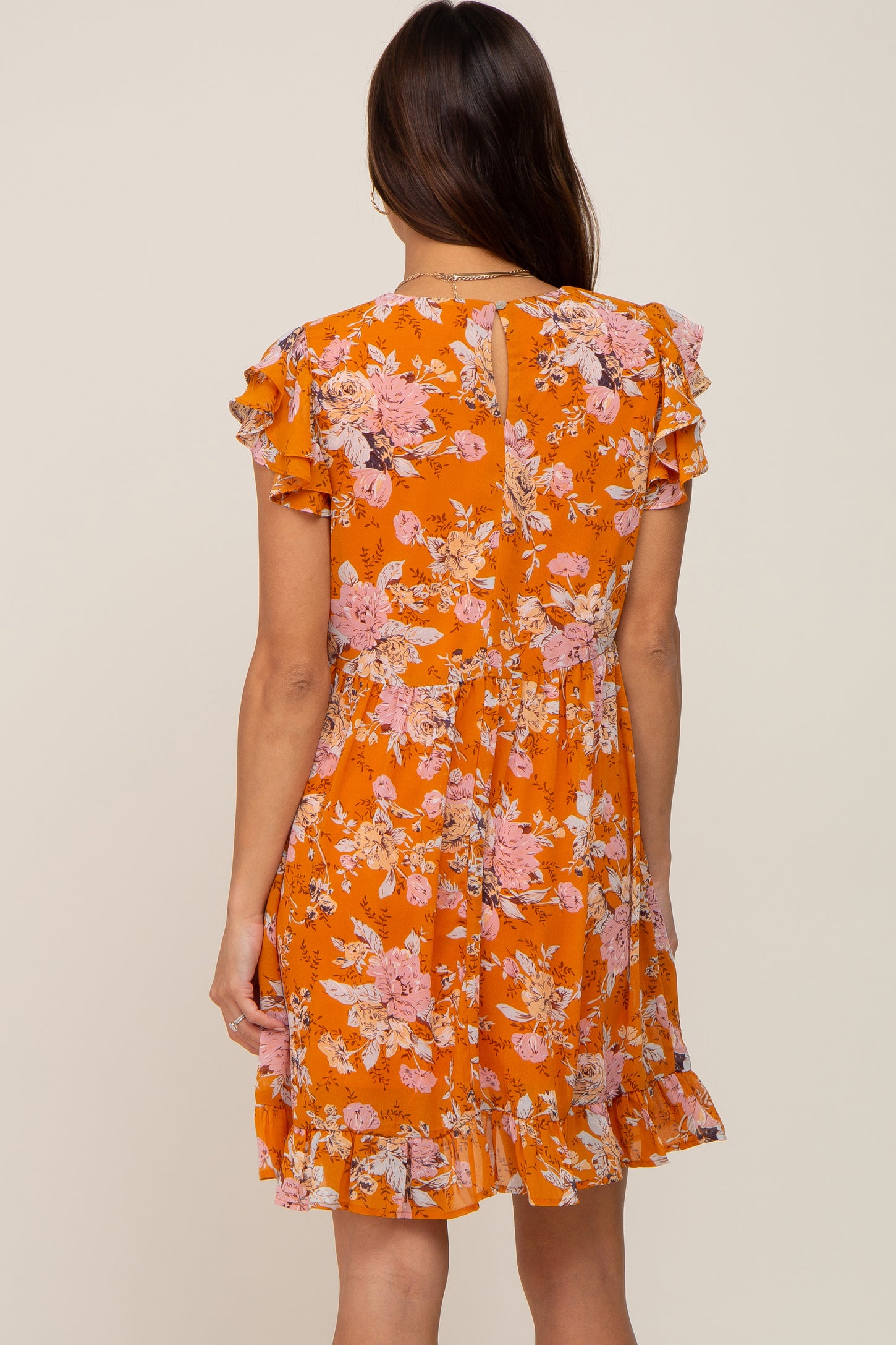 Back view of woman wearing orange floral mini dress with ruffle sleeves and hem