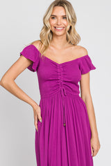 woman wearing a bright purple off-the-shoulder dress with smocked bodice and ruffled sleeves, smiling at the camera