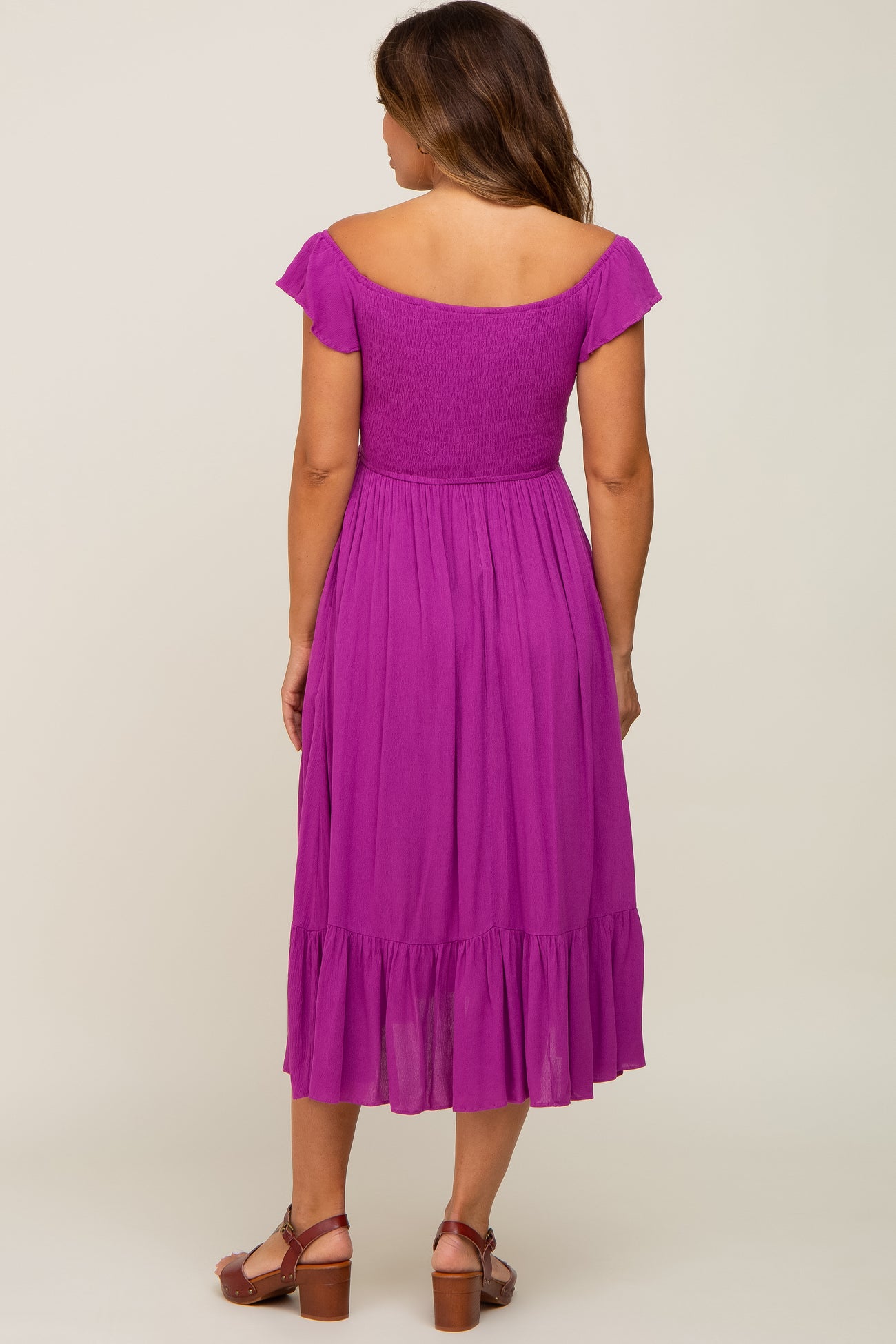 woman wearing a back view of a purple short sleeve maternity dress with a ruffled hemline