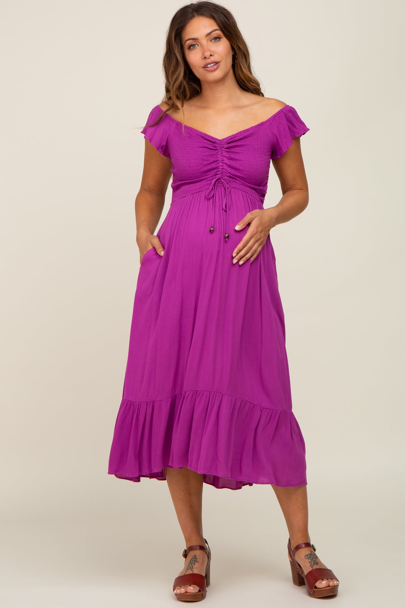 woman wearing a purple off-the-shoulder maternity dress with smocked bodice and ruffle hem, showcasing her baby bump