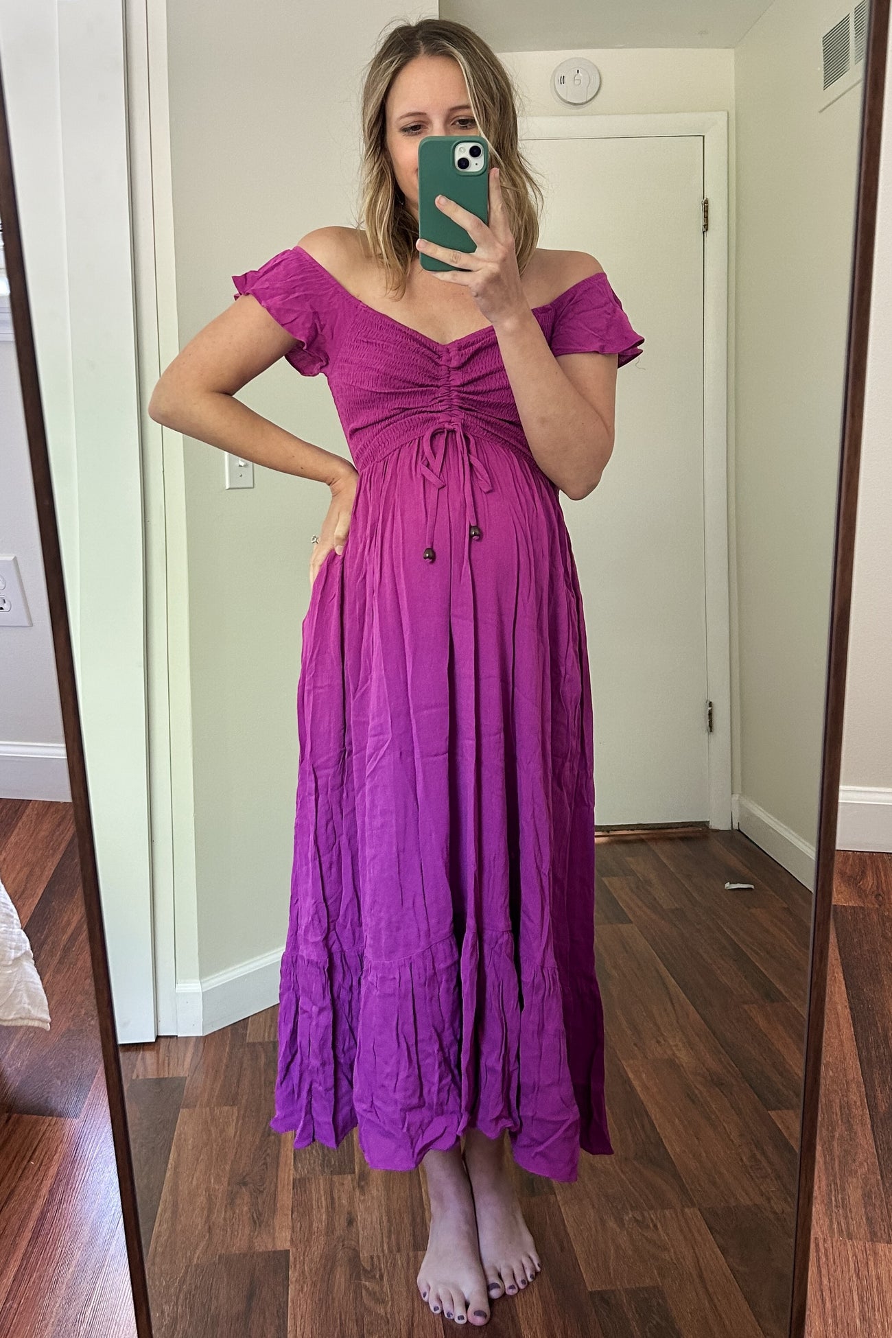 woman wearing a pink off-the-shoulder maternity dress with a tie front and a visible baby bump