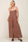 Woman wearing a brown strapless wide-leg jumpsuit with a twisted bodice and black sandals