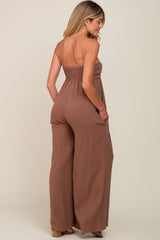 woman wearing a brown strapless smocked maternity jumpsuit with wide legs and pockets