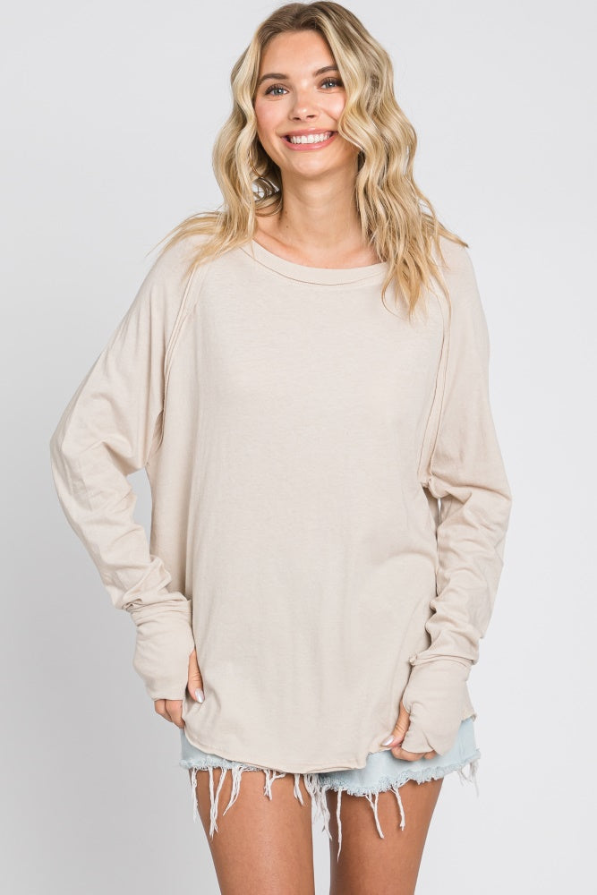 woman wearing a beige long sleeve oversized top with rolled cuffs and distressed denim shorts