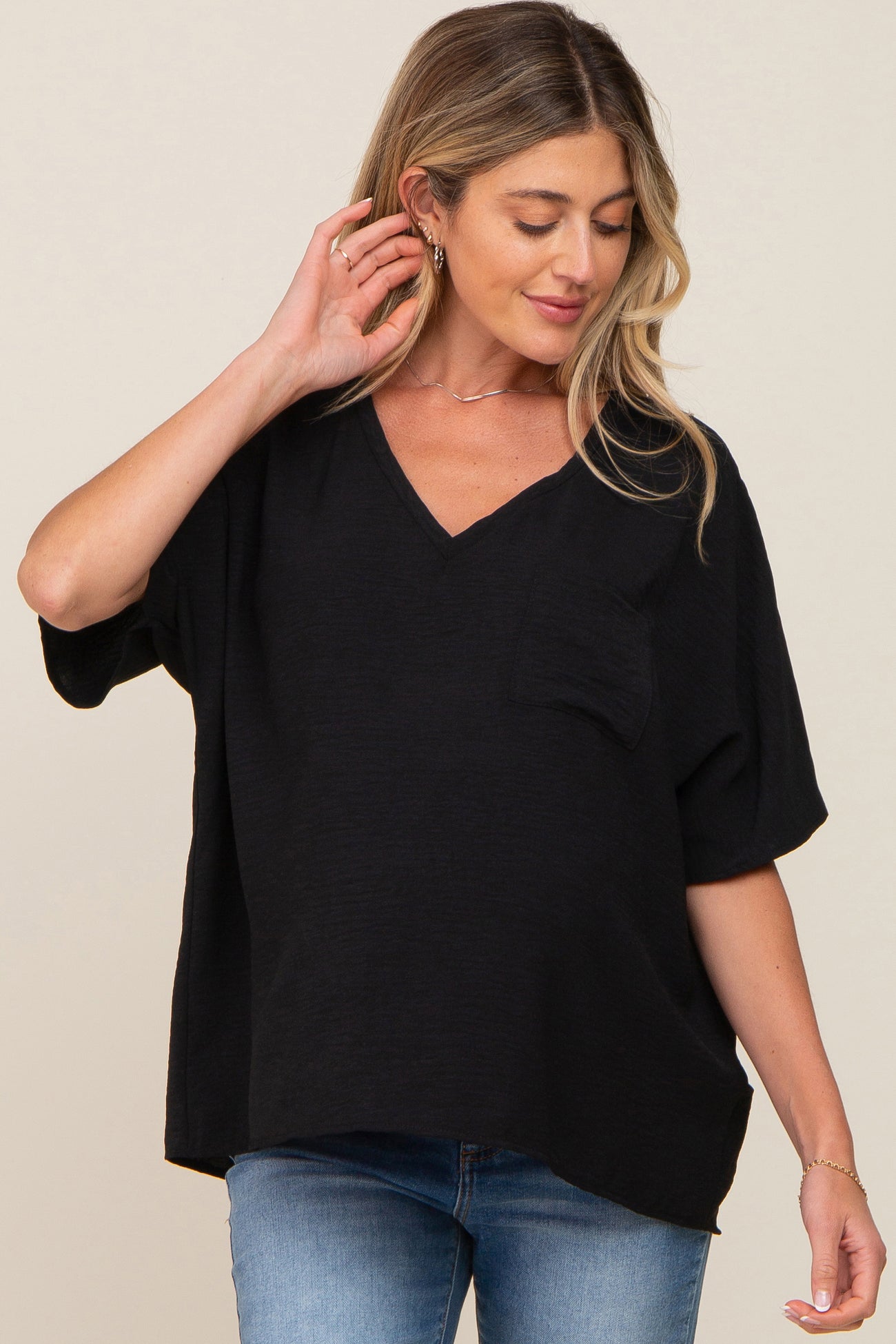 woman wearing a black v-neck maternity top with a pocket and loose fit, showcasing her baby bump