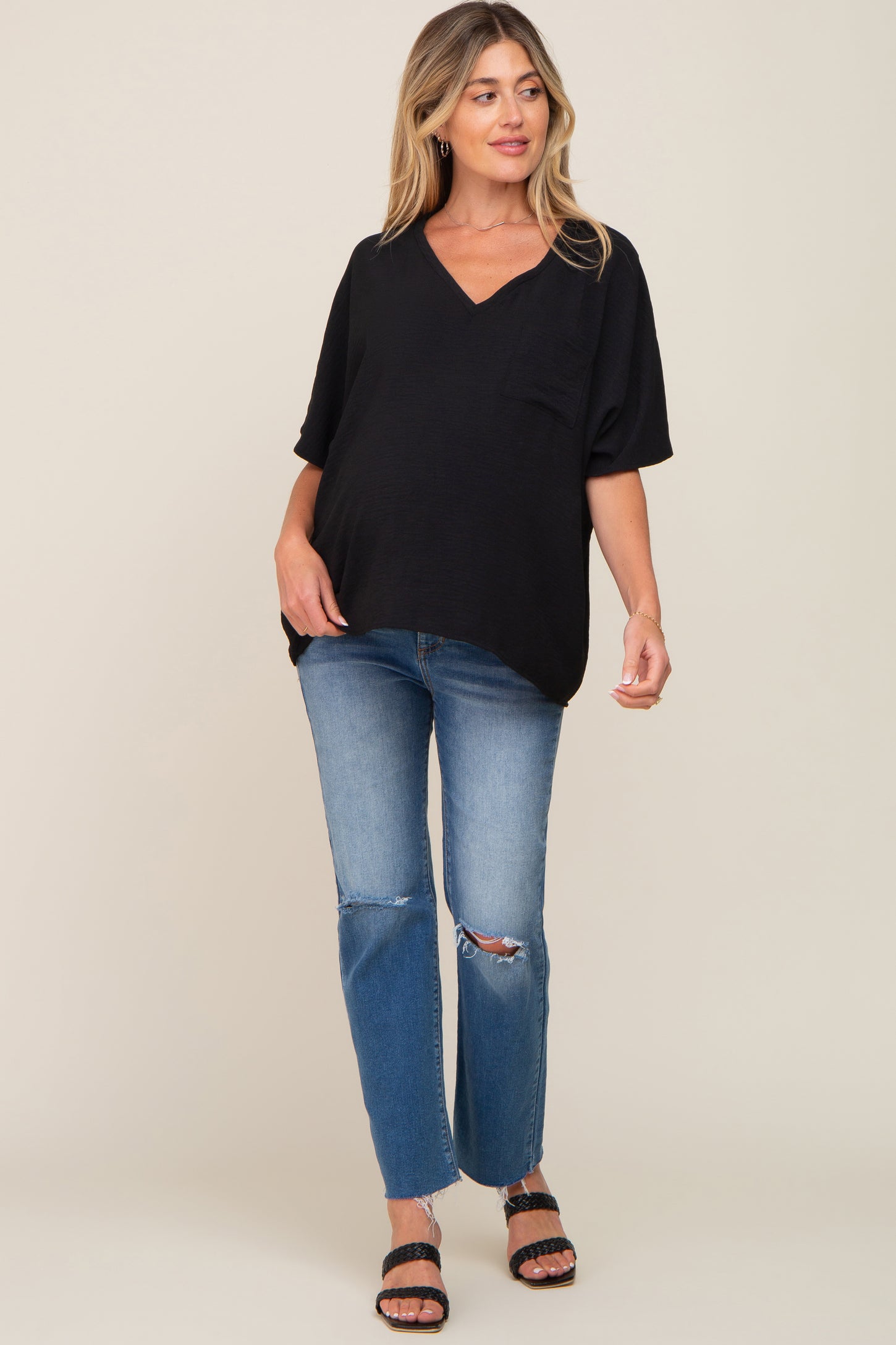 woman wearing a black v-neck maternity top with a pocket, paired with distressed jeans and sandals, showing her baby bump