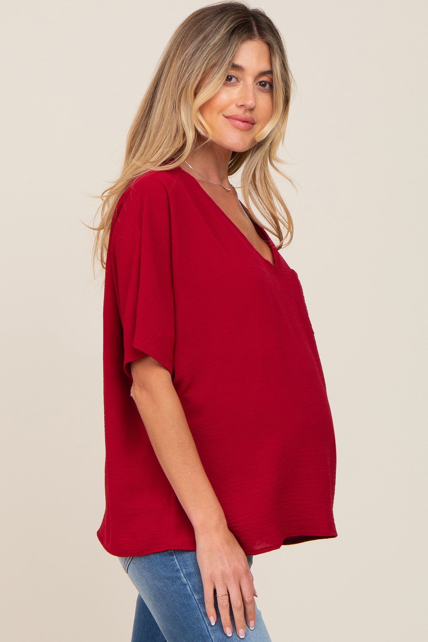 woman wearing a deep red maternity top with a v-neck and relaxed fit, showcasing a visible baby bump