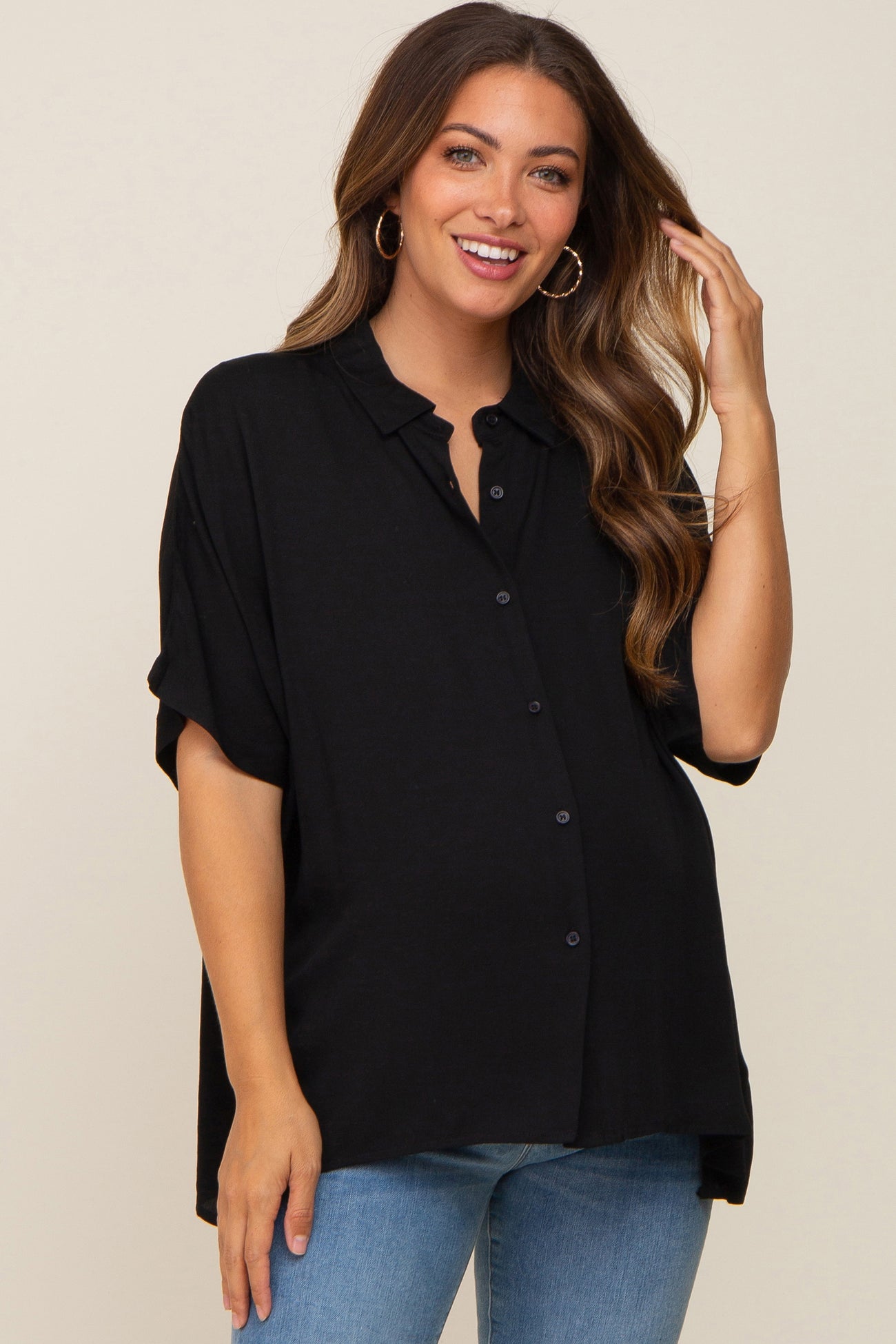 smiling woman wearing a black short sleeve button down maternity top and blue jeans