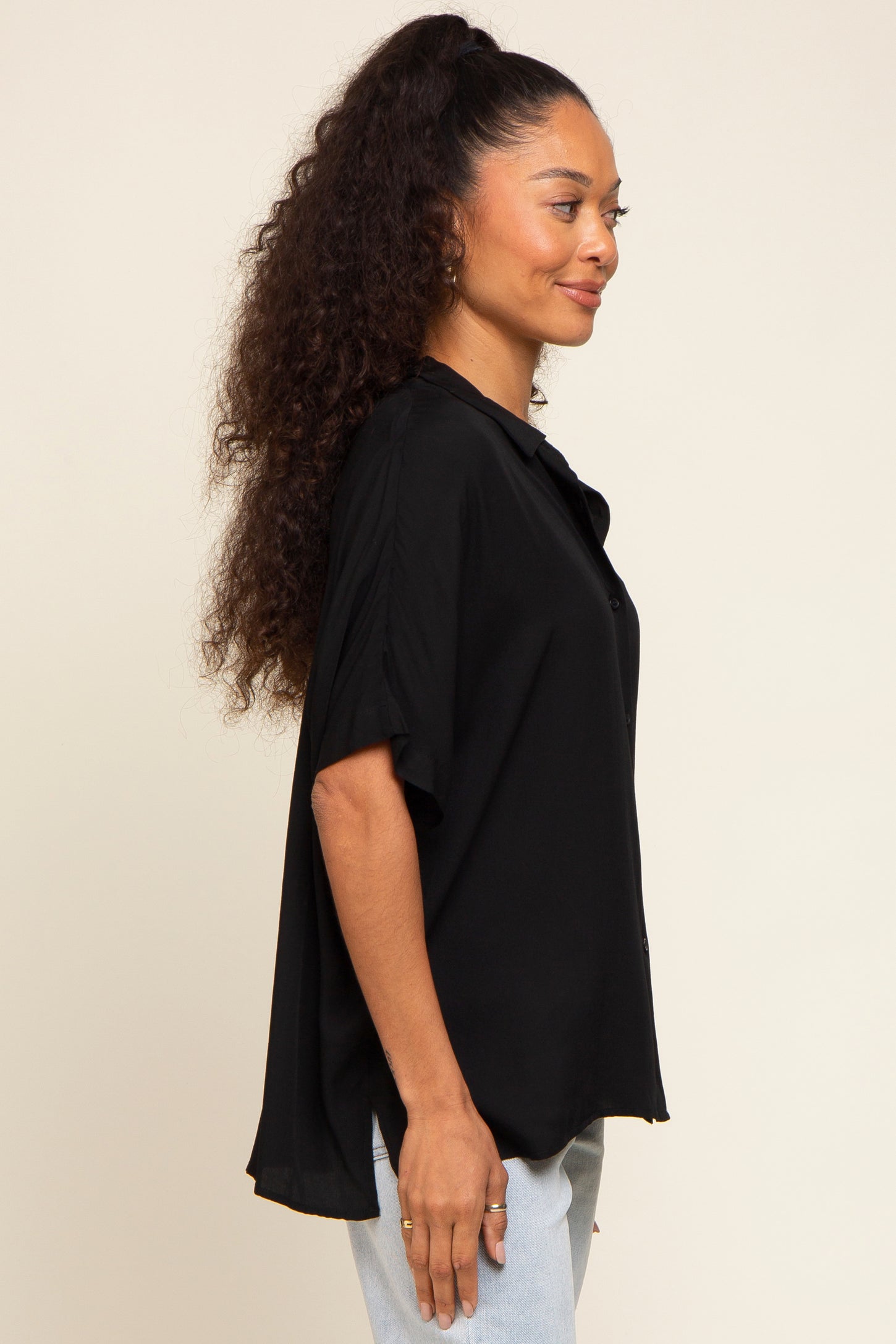 woman wearing a black short sleeve button-up shirt with a loose fit and side slits, styled with light blue jeans