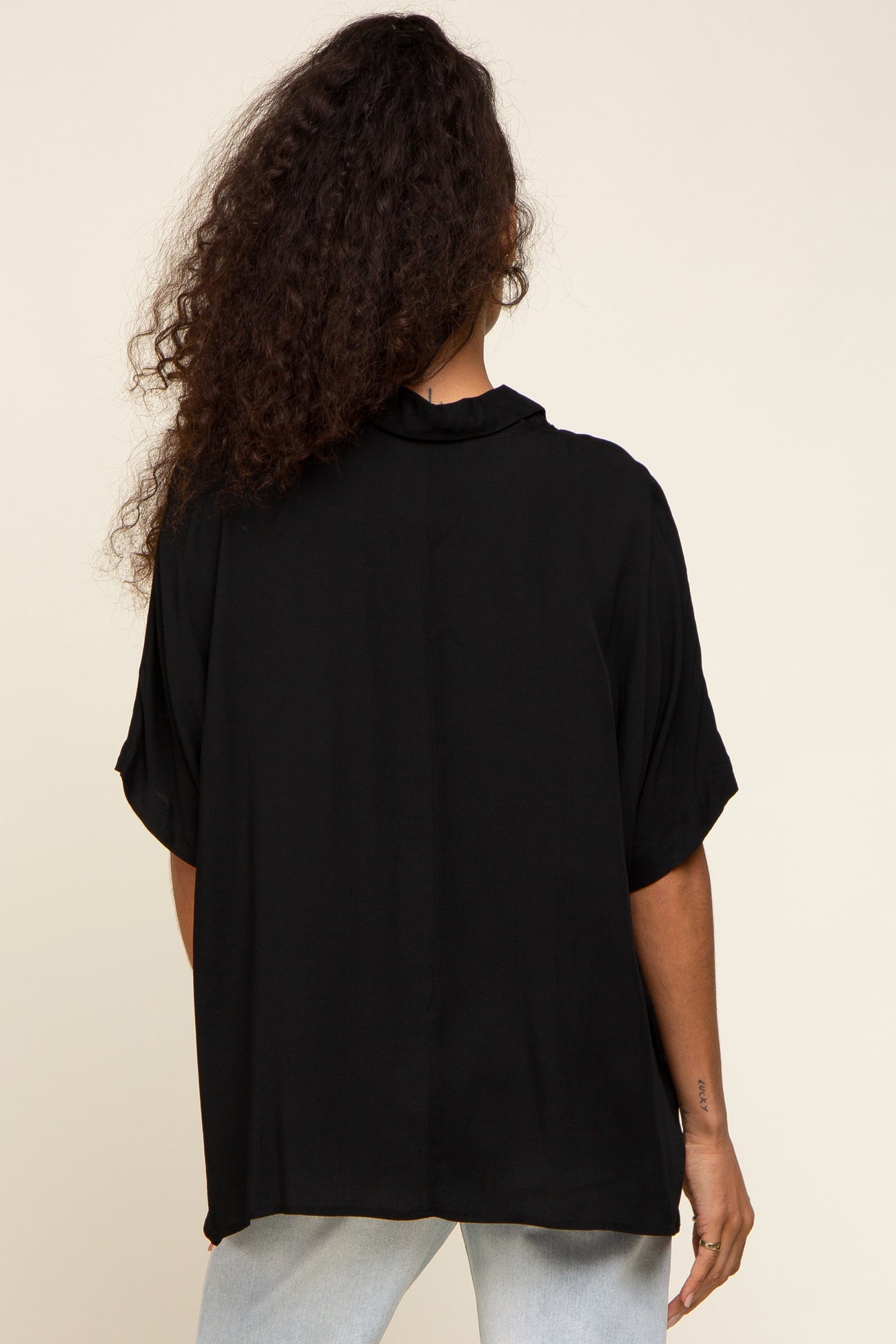 woman wearing a loose-fitting black blouse with short sleeves and a collar, seen from the back
