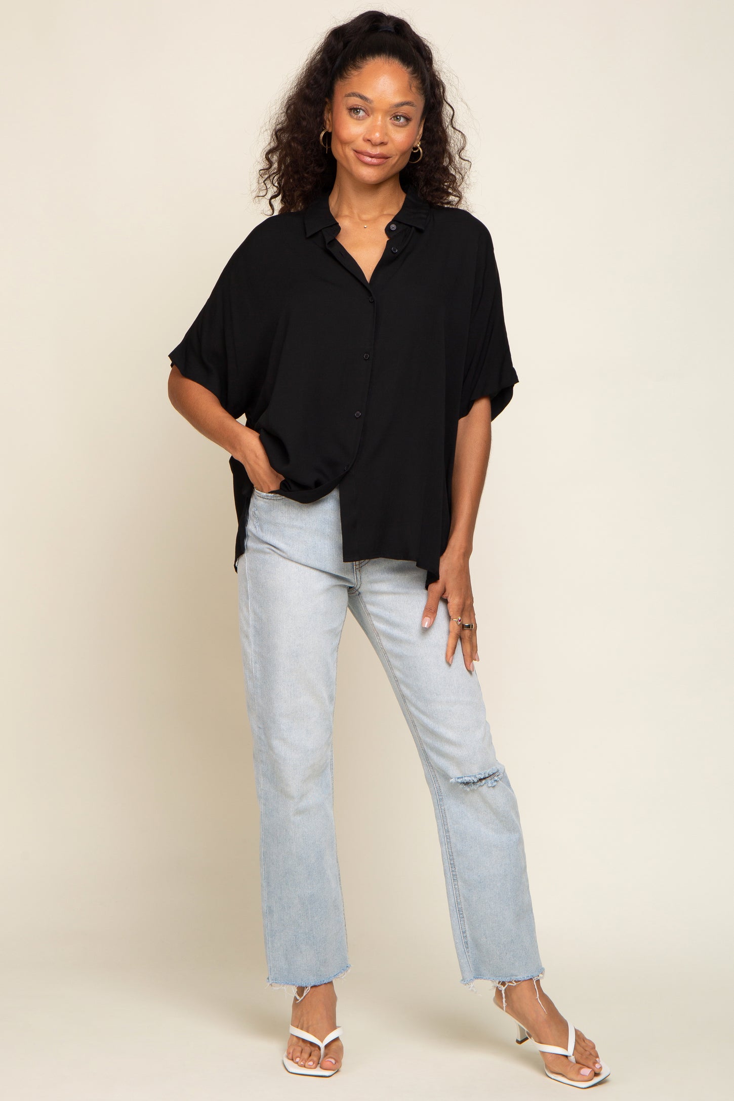 Woman wearing a black short-sleeve button-down shirt and light wash distressed jeans with white sandals